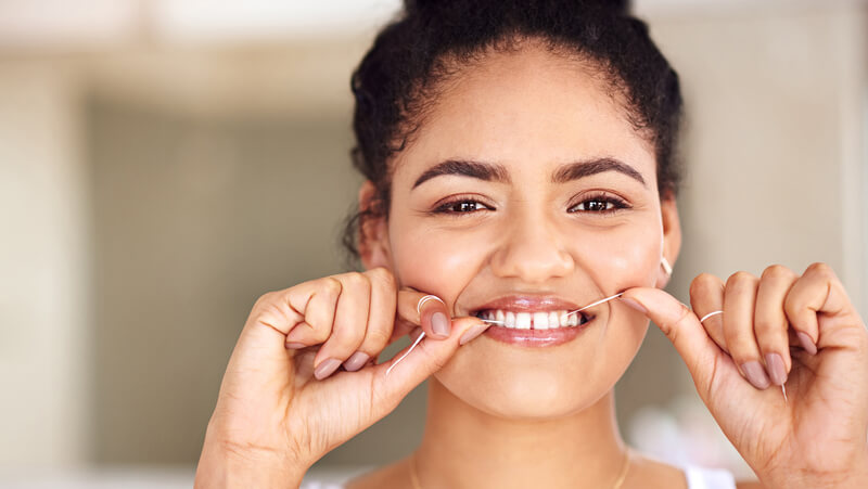 Young woman smiling while flossing teeth.